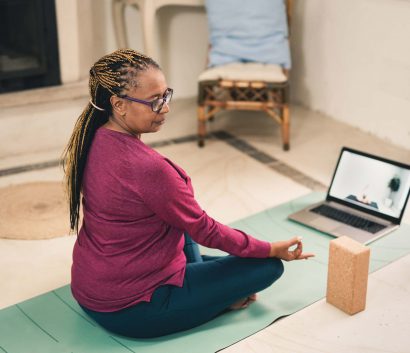 An African-American woman sitting on the floor doing yoga; she is facing a laptop computer