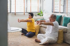 Asian old senior workout exercise and doing yoga at home An older Asian couple sits on the floor doing stretching exercises with their hands and arms.