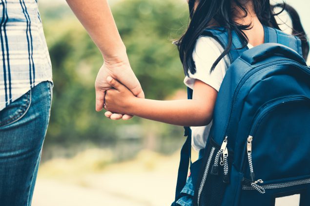A father walks his daughter to school; the young girl is wearing a backpack.
