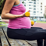 A pregnant woman exercises with hand weights.
