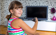 A young girl points a remote control at a flat panel TV monitor