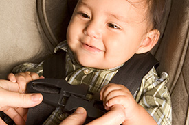 An infant being buckled in to a child safety seat.
