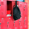 A black backpack hangs from the open door of a red school locker